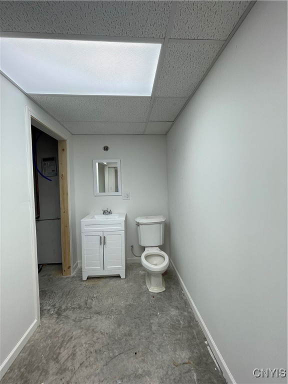 bathroom featuring concrete flooring, vanity, a drop ceiling, and toilet