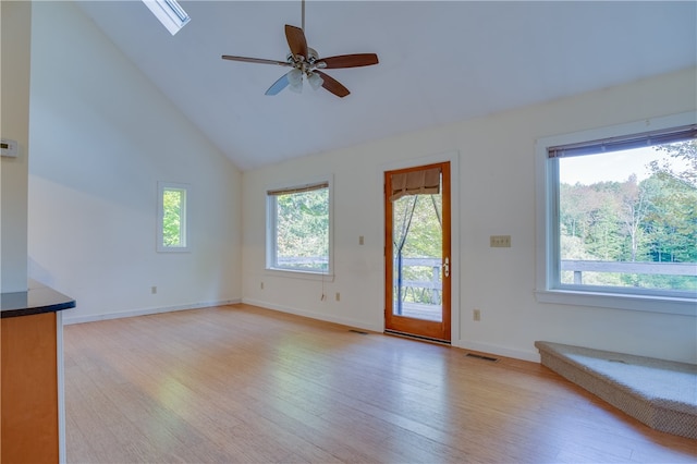 unfurnished living room with light hardwood / wood-style floors, ceiling fan, a skylight, and high vaulted ceiling