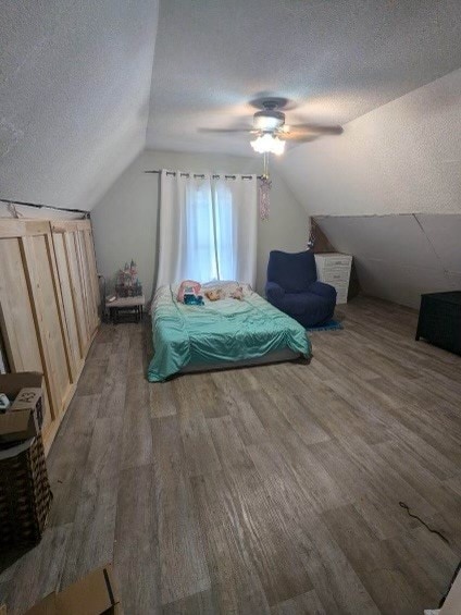 bedroom with lofted ceiling, a textured ceiling, hardwood / wood-style flooring, and ceiling fan