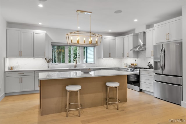 kitchen featuring stainless steel appliances, light wood-type flooring, wall chimney range hood, and a kitchen island