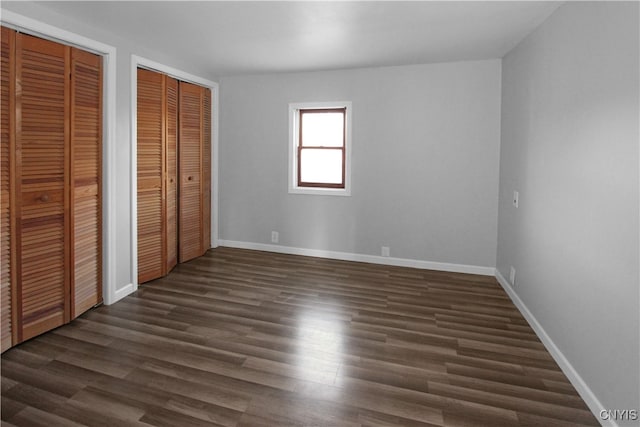 unfurnished bedroom with dark hardwood / wood-style flooring and two closets