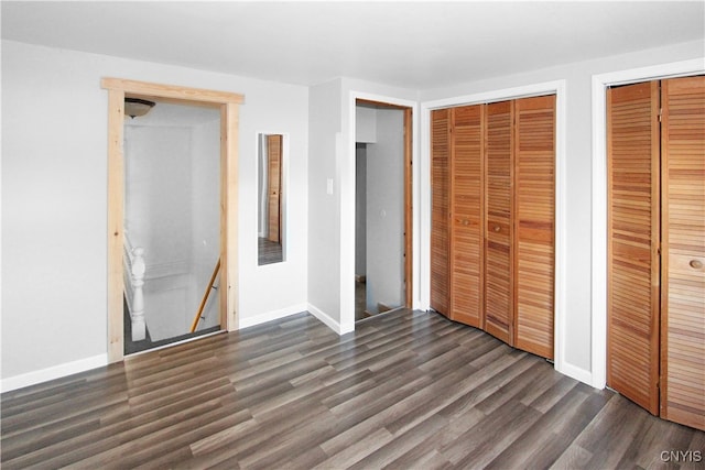 unfurnished bedroom with dark hardwood / wood-style floors and multiple closets