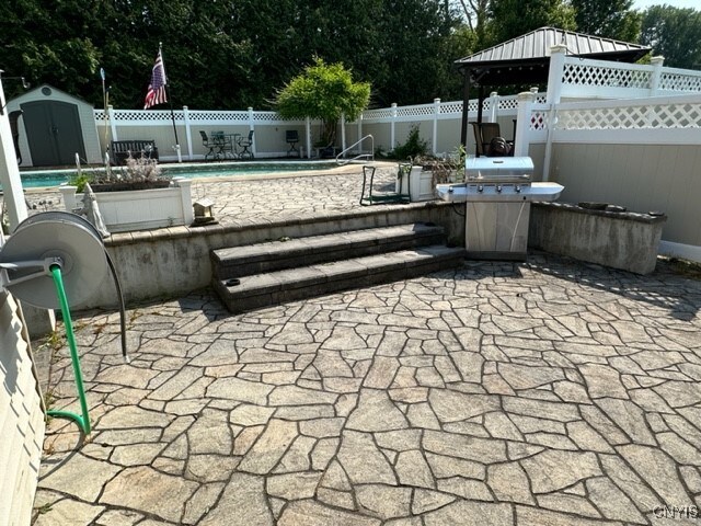 view of patio with a shed, a fenced in pool, and a grill