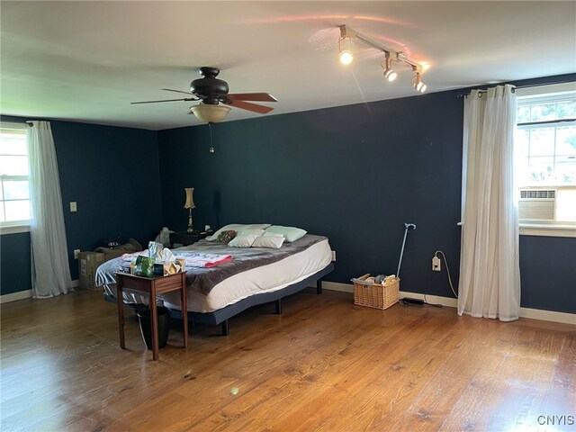 bedroom featuring multiple windows, hardwood / wood-style flooring, cooling unit, and ceiling fan