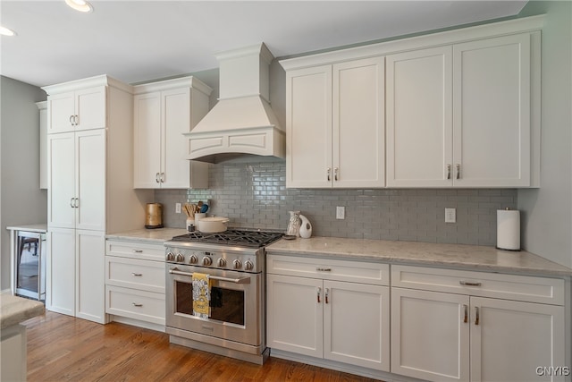 kitchen featuring backsplash, custom exhaust hood, high end stove, beverage cooler, and light hardwood / wood-style flooring