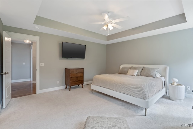 bedroom featuring light colored carpet, a raised ceiling, and ceiling fan