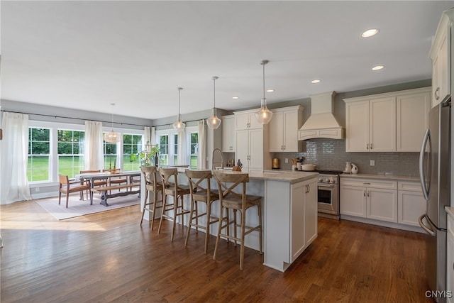 kitchen featuring hanging light fixtures, dark hardwood / wood-style floors, an island with sink, custom range hood, and stainless steel appliances