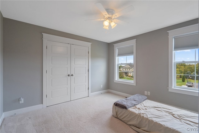 bedroom featuring a closet, light colored carpet, multiple windows, and ceiling fan