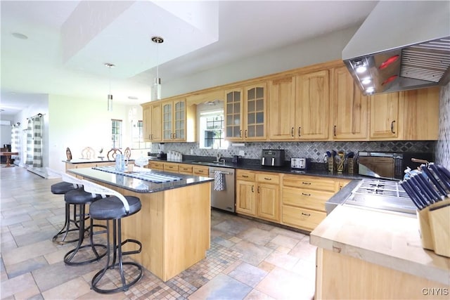 kitchen with hanging light fixtures, backsplash, extractor fan, a center island with sink, and appliances with stainless steel finishes