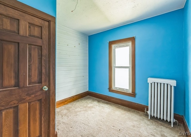 unfurnished room featuring radiator heating unit, wood walls, and light colored carpet