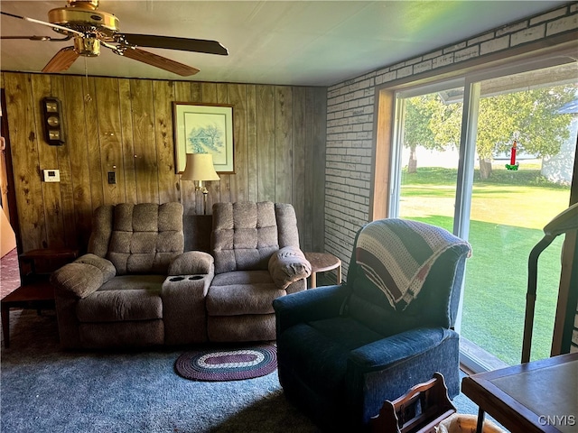 living room with ceiling fan, carpet floors, wooden walls, and brick wall