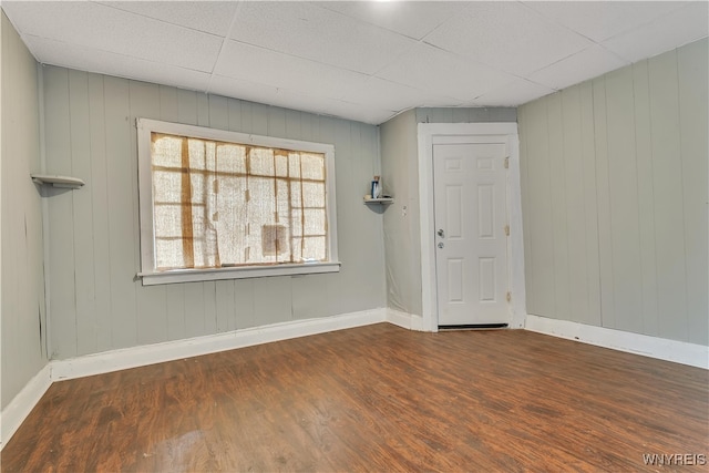 spare room featuring a drop ceiling, wood walls, and dark hardwood / wood-style flooring