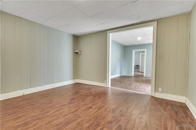 empty room with a drop ceiling, wooden walls, and dark wood-type flooring