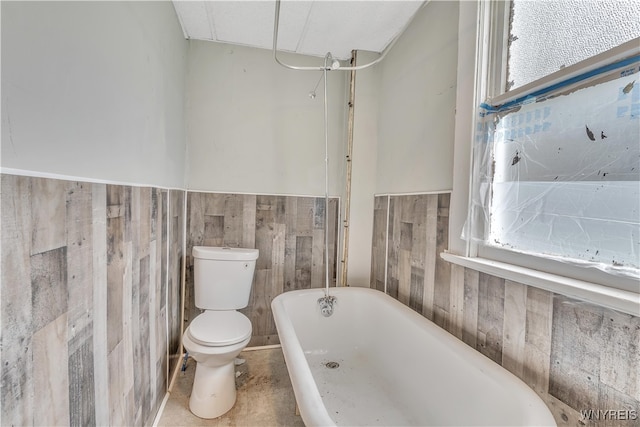 bathroom featuring wooden walls, a bath, a healthy amount of sunlight, and toilet