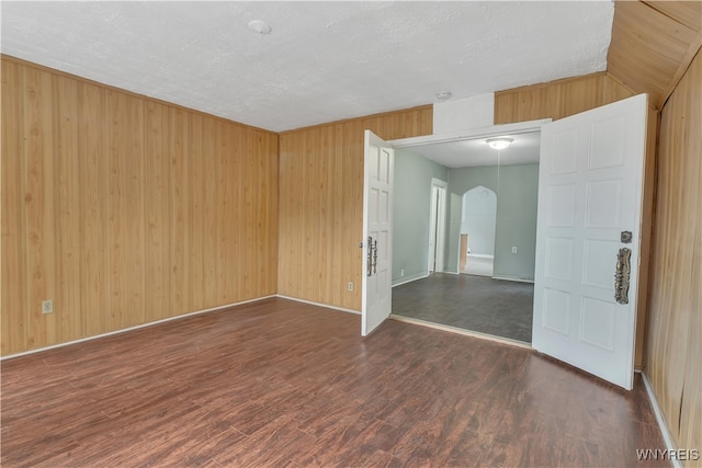 unfurnished room featuring a textured ceiling, wood walls, and dark wood-type flooring