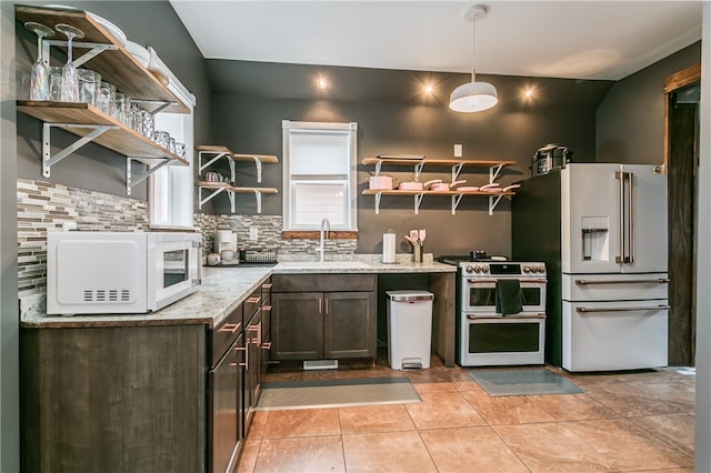 kitchen featuring light stone counters, hanging light fixtures, sink, white appliances, and dark brown cabinets