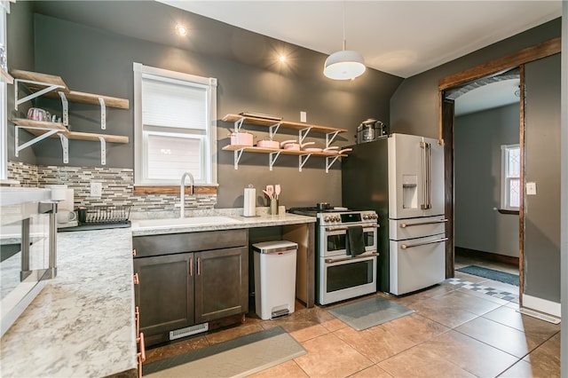 kitchen featuring light stone counters, pendant lighting, light tile patterned floors, sink, and premium appliances