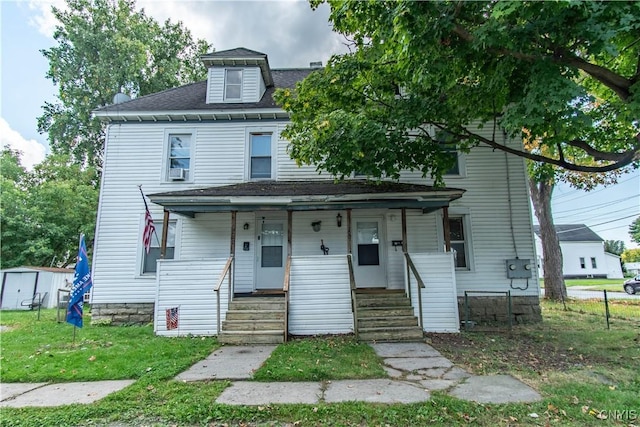 traditional style home with covered porch, a shingled roof, and a front yard