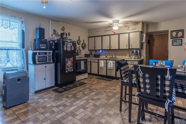 kitchen with light countertops, ceiling fan, stainless steel microwave, range with gas cooktop, and freestanding refrigerator
