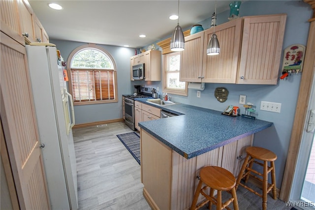 kitchen featuring appliances with stainless steel finishes, hanging light fixtures, a kitchen breakfast bar, light brown cabinets, and light hardwood / wood-style flooring