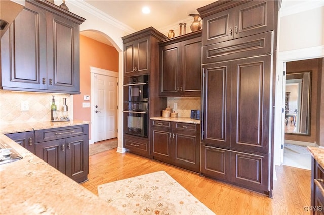 kitchen with black double oven, light hardwood / wood-style flooring, decorative backsplash, light stone counters, and dark brown cabinetry