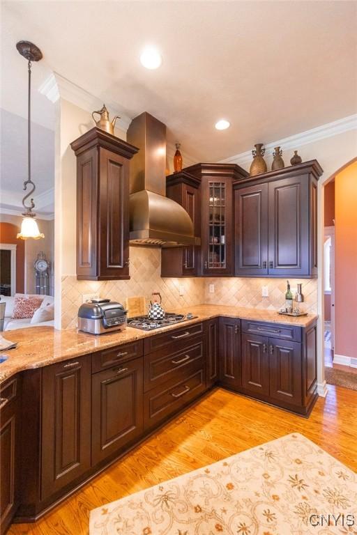 kitchen with ornamental molding, wall chimney exhaust hood, stainless steel gas cooktop, pendant lighting, and light hardwood / wood-style flooring