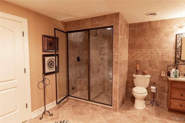 bathroom featuring tile patterned floors, toilet, a shower with door, vanity, and tile walls