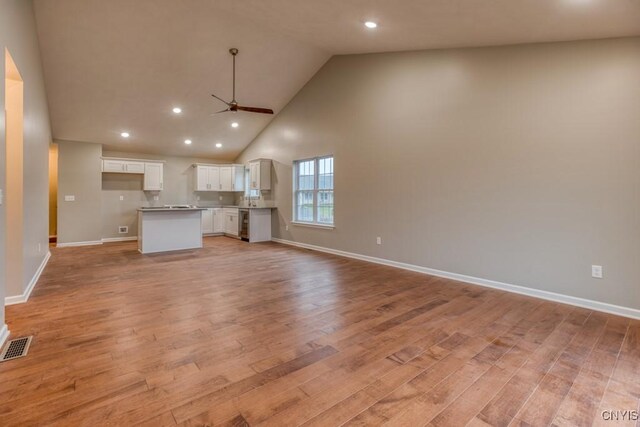 unfurnished living room with high vaulted ceiling, light wood-type flooring, and ceiling fan