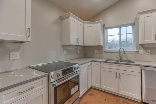 kitchen featuring light hardwood / wood-style floors, sink, vaulted ceiling, white cabinetry, and stainless steel appliances