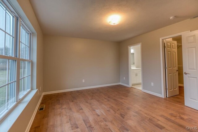 unfurnished bedroom with light wood-type flooring, ensuite bath, multiple windows, and a walk in closet