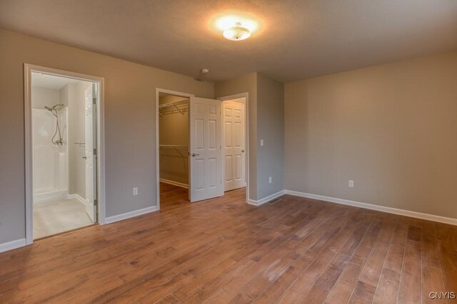 unfurnished bedroom with a textured ceiling, a closet, a spacious closet, ensuite bath, and hardwood / wood-style floors