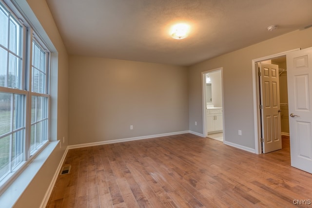 unfurnished bedroom featuring multiple windows, a spacious closet, light hardwood / wood-style flooring, and ensuite bathroom