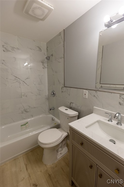 full bathroom with tile walls, wood-type flooring, vanity, tiled shower / bath, and toilet