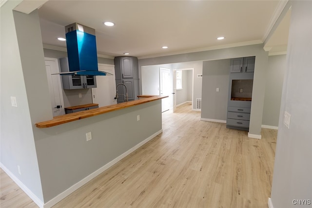 kitchen with gray cabinetry, light hardwood / wood-style floors, island range hood, and butcher block counters