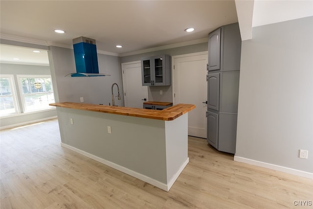 kitchen featuring gray cabinetry, butcher block counters, ventilation hood, light hardwood / wood-style flooring, and ornamental molding