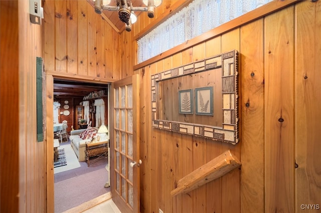 hallway featuring a towering ceiling, light colored carpet, and wood walls