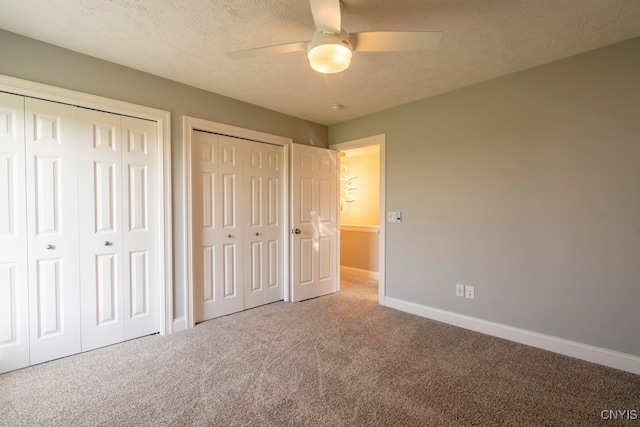 unfurnished bedroom with ceiling fan, a textured ceiling, carpet floors, and two closets