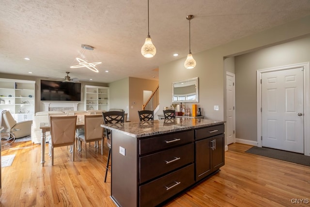 kitchen featuring a breakfast bar area, light wood-type flooring, a textured ceiling, dark brown cabinets, and ceiling fan