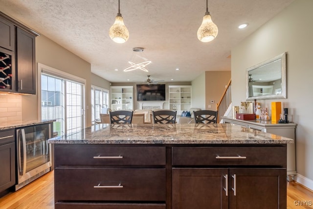 kitchen featuring dark brown cabinetry, wine cooler, hanging light fixtures, and light hardwood / wood-style floors