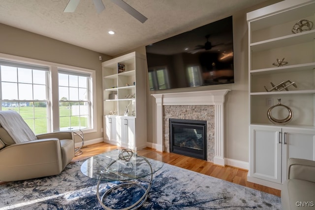 living room with light wood-type flooring, a stone fireplace, and ceiling fan