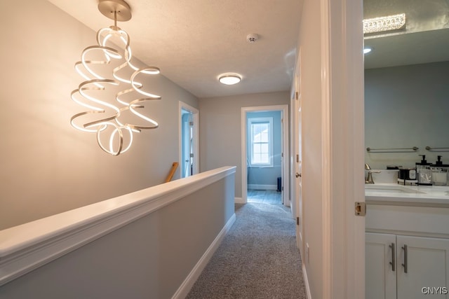 hall featuring a textured ceiling, light carpet, sink, and a chandelier