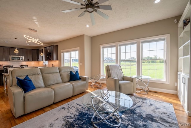 living room with a textured ceiling, a healthy amount of sunlight, ceiling fan, and light hardwood / wood-style flooring