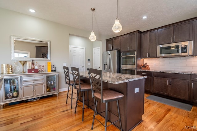 kitchen featuring dark brown cabinets, light hardwood / wood-style flooring, stainless steel appliances, and a breakfast bar