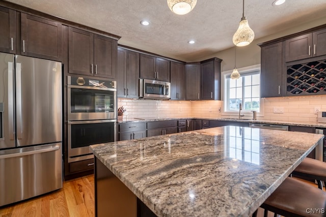 kitchen featuring appliances with stainless steel finishes, a kitchen island, light stone countertops, and decorative light fixtures