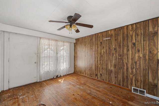 spare room featuring hardwood / wood-style flooring, ceiling fan, and wood walls