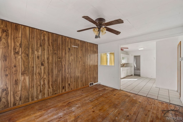 empty room featuring wooden walls, ceiling fan, and light wood-type flooring