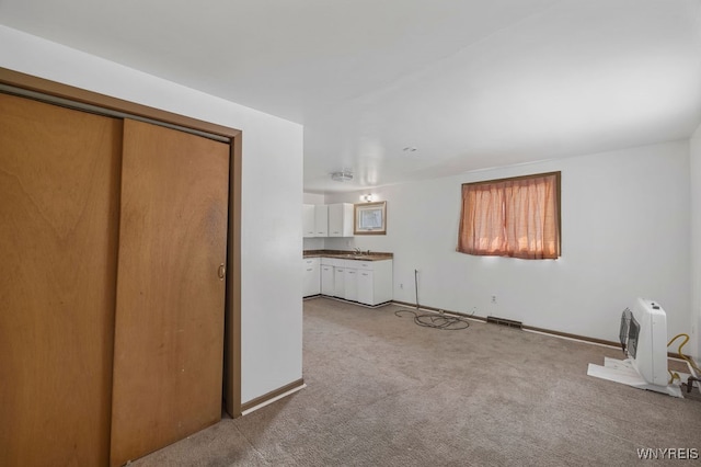 unfurnished living room with heating unit, sink, and light colored carpet