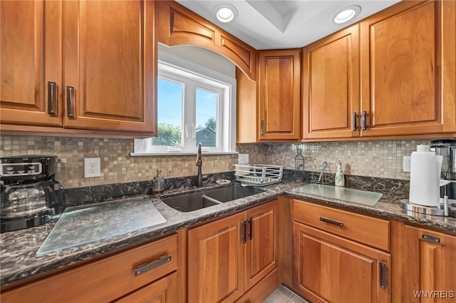 kitchen featuring dark stone countertops, light tile patterned floors, backsplash, and sink