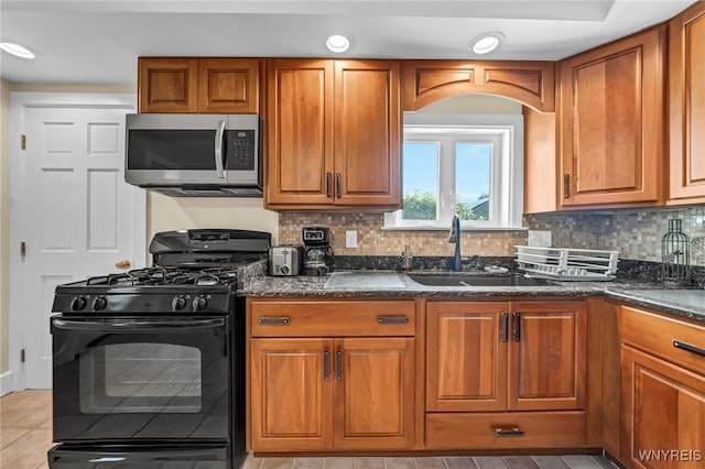 kitchen featuring dark stone countertops, black range with gas stovetop, sink, and decorative backsplash