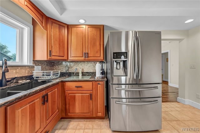 kitchen with light tile patterned flooring, sink, backsplash, dark stone countertops, and stainless steel fridge